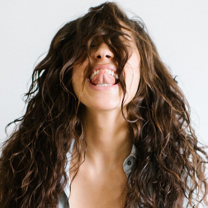 Mujer con largo cabello castaño y rizado sacando la lengua