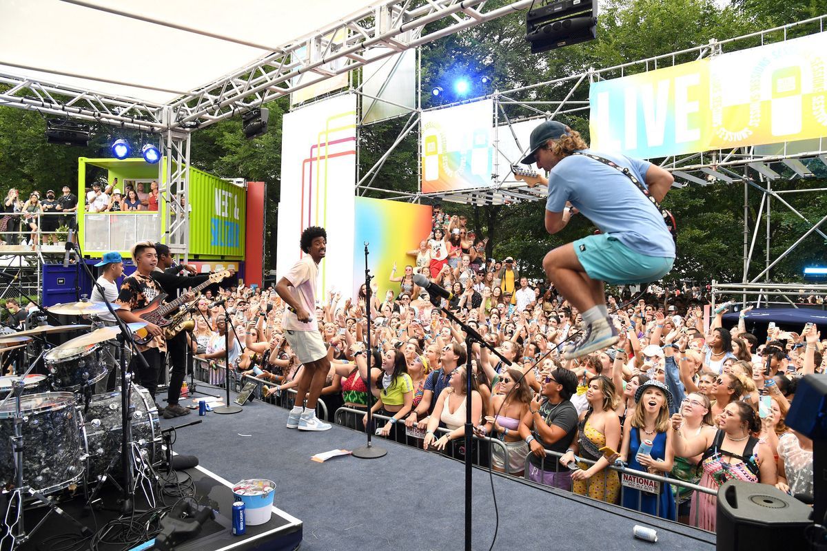 Ein Musiker springt mit einer Gitarre hoch in die Luft, während ein Publikum eine Aufführung im Lollapalooza aufnimmt.