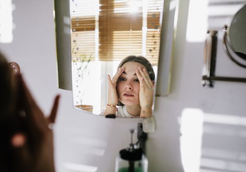Vrouw die in spiegel kijkt terwijl haar gezicht tot een kom vormt.