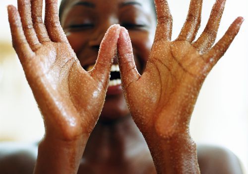 Sorridente donna di colore esfoliante con uno scrub per il corpo