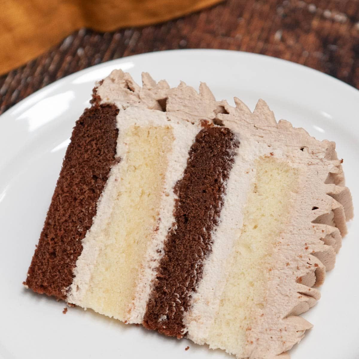 פרוסת עוגת שוקולד וניל עם קצפת שוקולד על צלחת לבנה