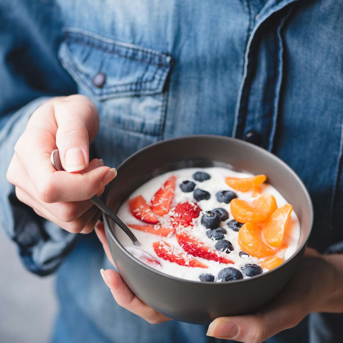 mulher em uma camisa jeans comendo uma tigela de iogurte e frutas