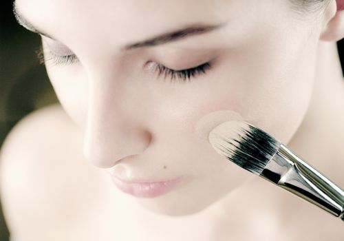 Ung kvinde, der anvender fundament på kinden med make-up børste, close-up
