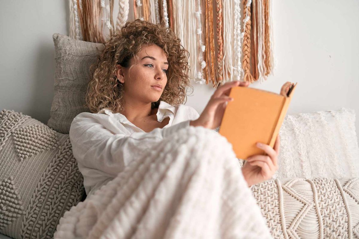 Kvinde læser bog i sengen.