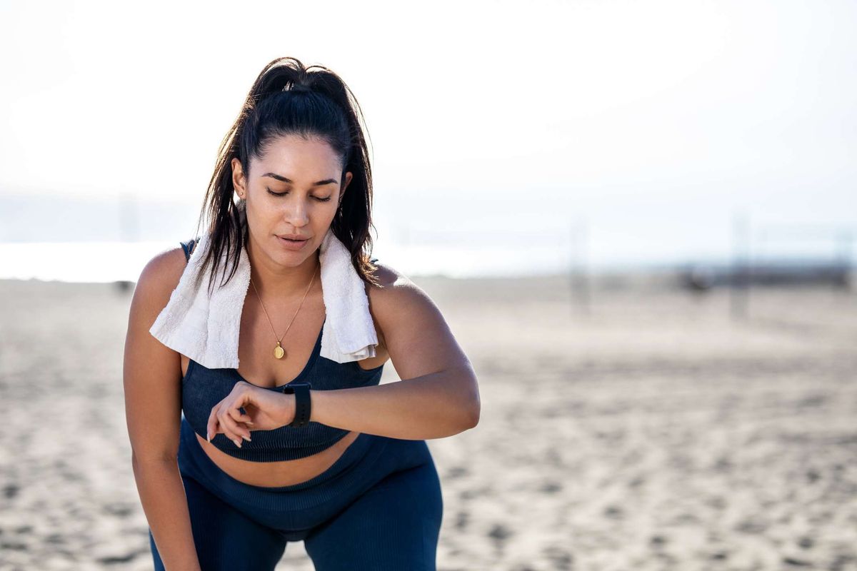kvinde, der kontrollerer fitnessur, mens du arbejder på stranden