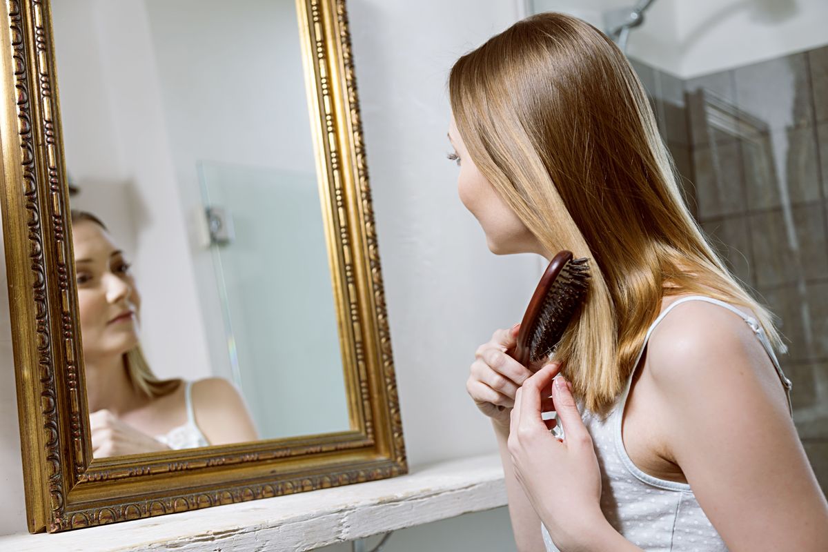 Mujer mirando en el espejo cepillarse el cabello