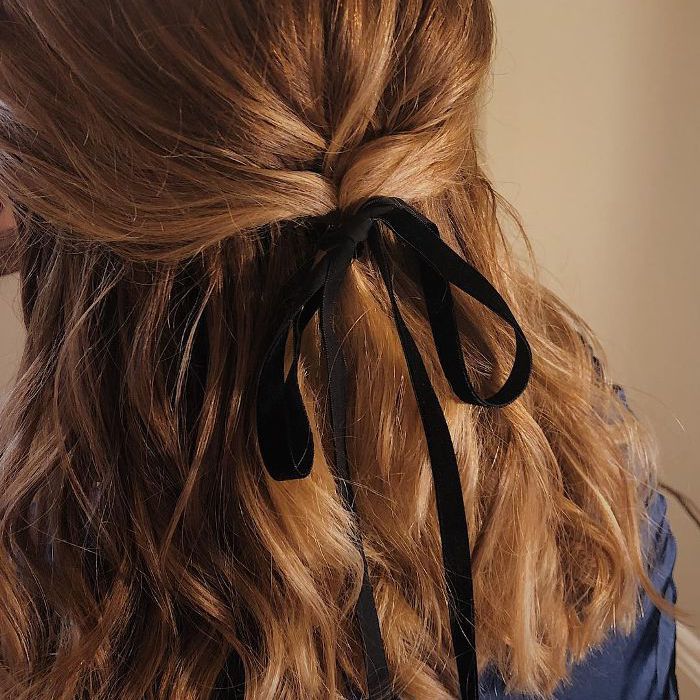 Mujer con cabello castaño recogido hasta la mitad y atado con una cinta negra