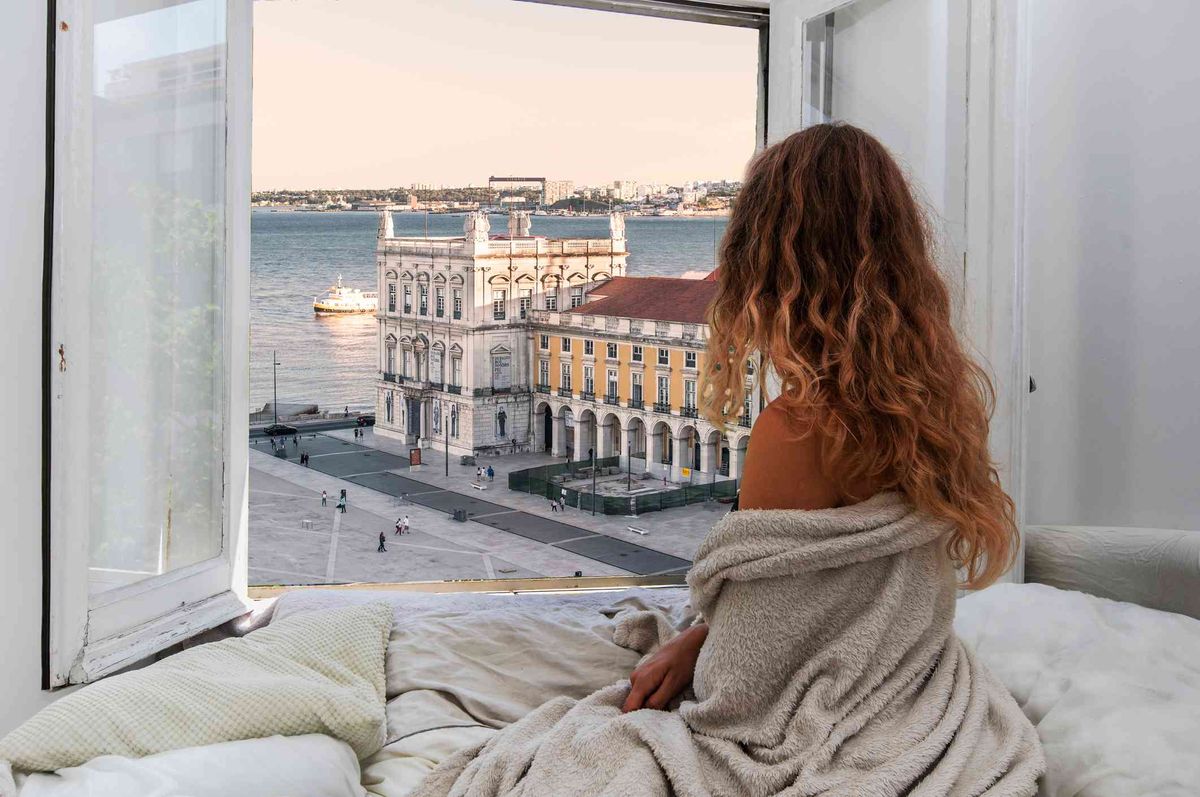 Mujer mirando por la ventana de su habitación de hotel a una hermosa vista