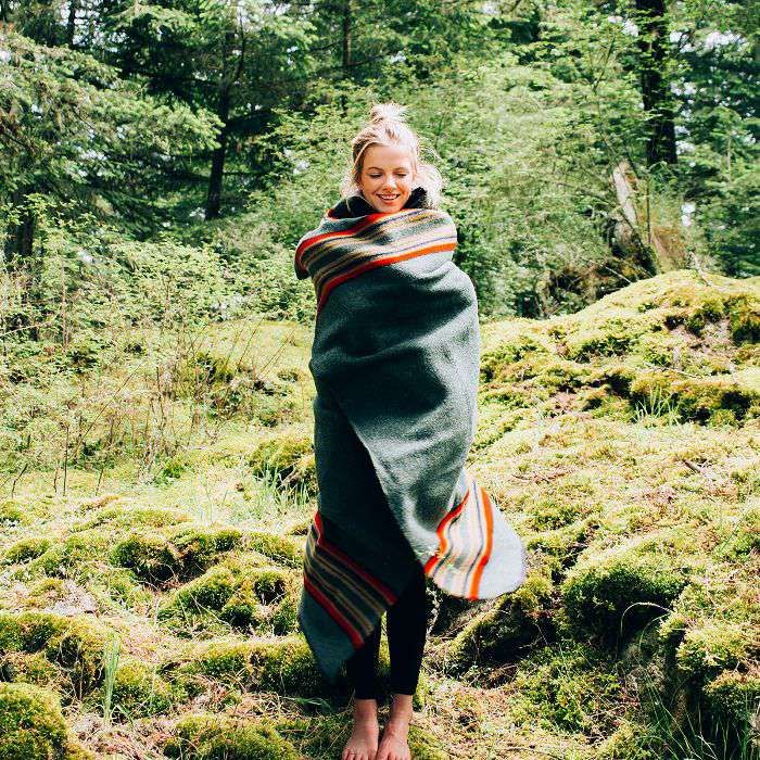 Mulher contente enrolada em um cobertor na floresta.