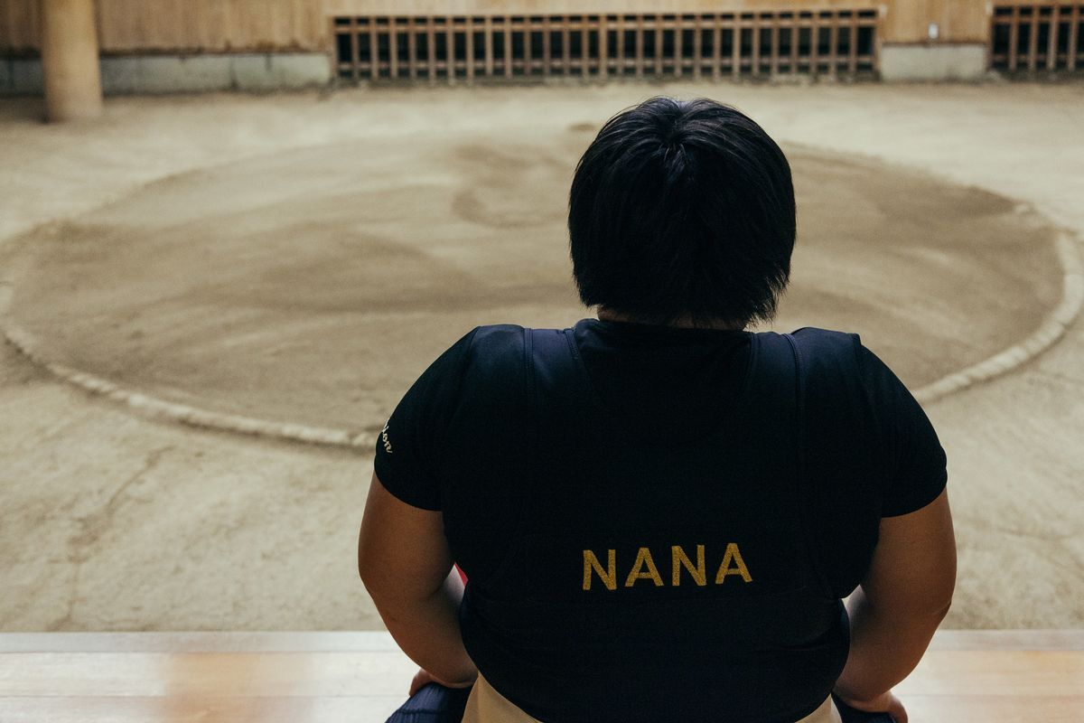 Ein junges Mädchen am Rand eines Sumo-Übungsrings trägt ein Hemd mit ihrem Namen darauf, Nana