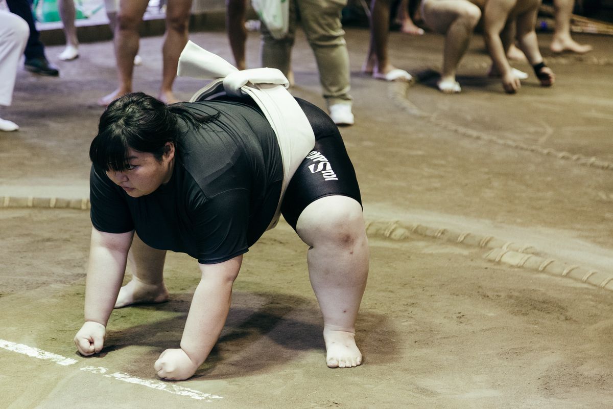 Eine junge Sumo-Ringerin kauert am Rand eines Rings