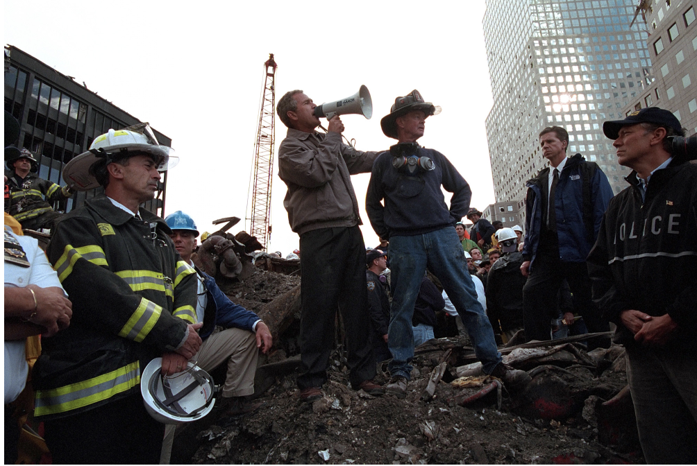 Президент Джордж Буш Дүниежүзілік сауда орталығының қирандыларының үстінде құтқарушылармен сөйлесіп жатқан өгізмен тұр