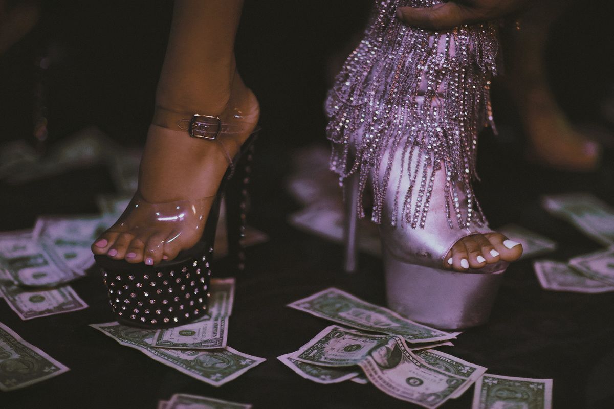 Dos mujeres con zapatos de tacón muy alto caminando sobre un piso lleno de dinero