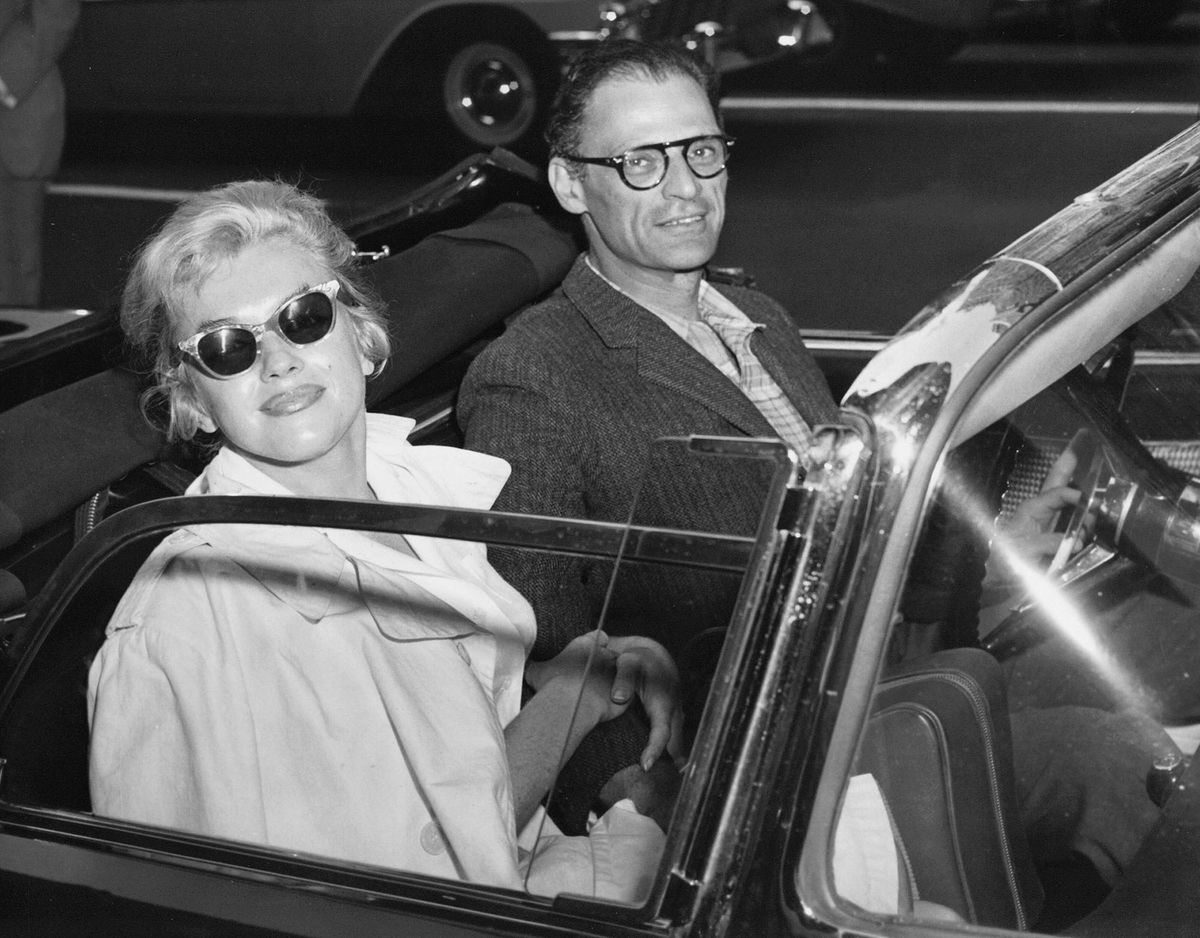 Marilyn Monroe mit Sonnenbrille lächelt vom Beifahrersitz eines Cabrios aus in die Kamera