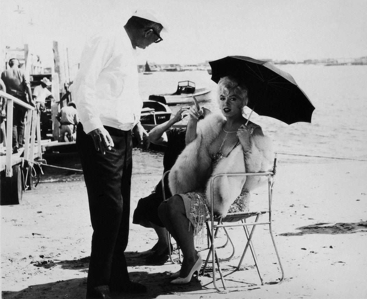 Marilyn Monroe auf einem Filmset unter einem Sonnenschirm im Gespräch mit dem Regisseur