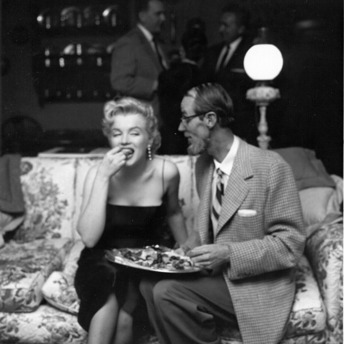 Marilyn Monroe isst und sitzt auf einer Couch neben einem Mann
