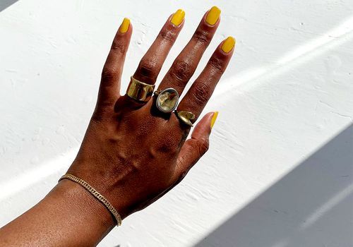 Hand mit Squoval Nägeln und goldenen Ringen