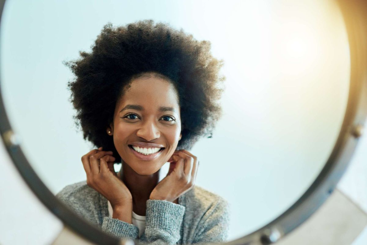 Schwarze Frau mit natürlichem Haar, das in den Spiegel schaut