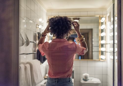 Kvinde, der fikser sit hår i spejlet på badeværelset