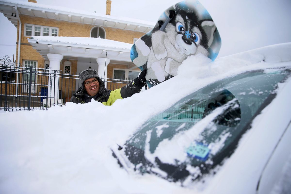 Ein lächelnder Mann, der Schnee von seinem Auto putzt