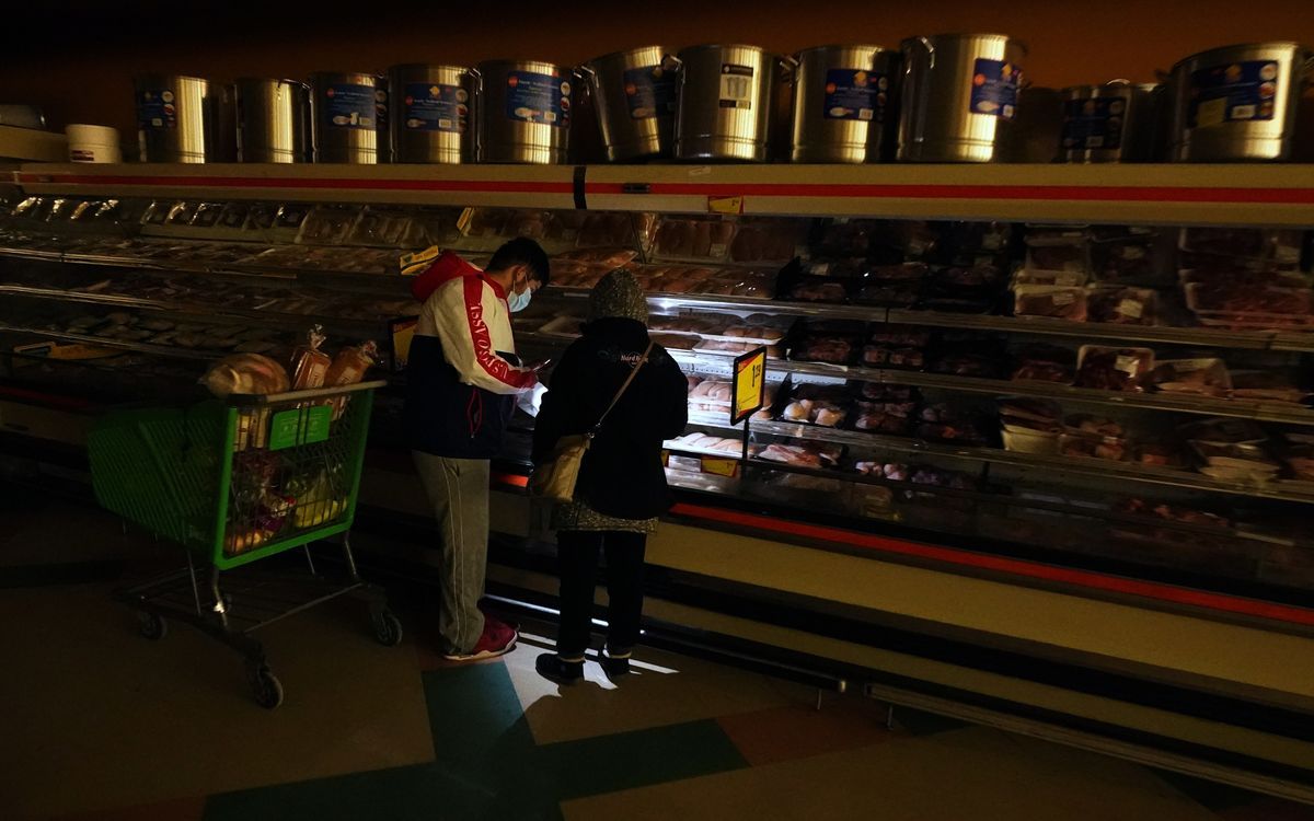Zwei Leute kaufen in einem Supermarkt mit Taschenlampe Fleisch, da der Strom ausfällt
