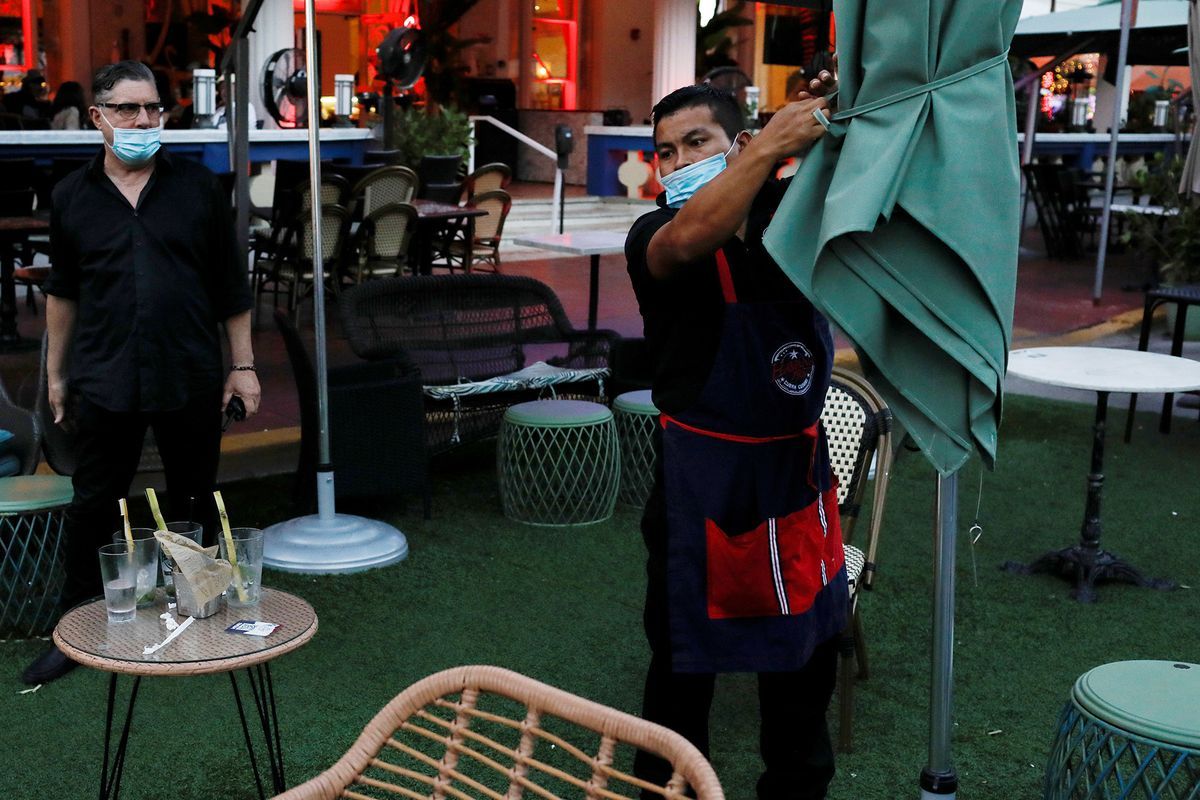마스크를 쓴 남자가 야외 식당에서 우산을 챙깁니다.