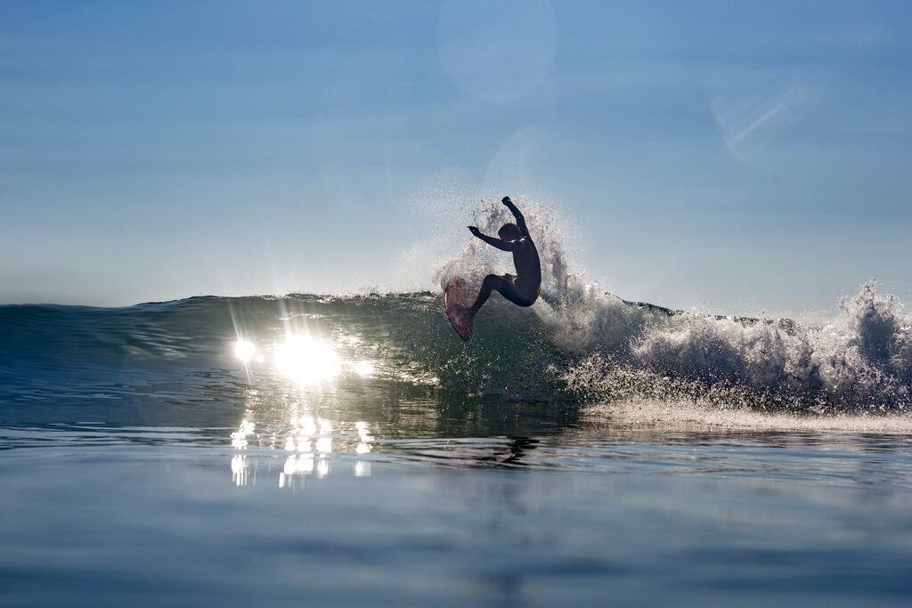 John John beim Surfen, schwebend in der Luft, während das Sonnenlicht auf das Wasser trifft