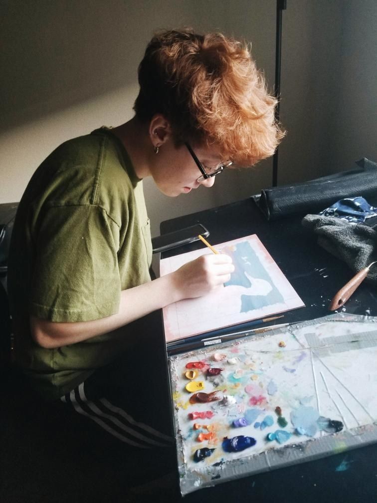 Umelec sedí nad kresliacim stolom s rôznymi farbami a hrubým náčrtom husacích kresieb