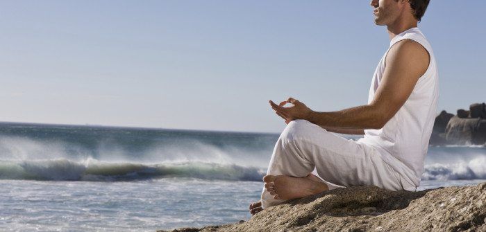 Komea nuori mies meditoi kalliota merellä