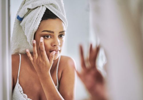 Frauen tragen im Spiegel Hautpflegecreme auf ihr Gesicht auf