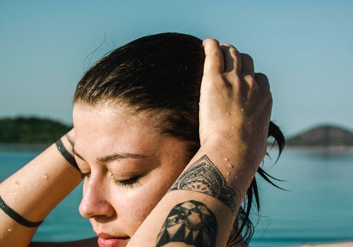 pige med vådt hår nær en vandkrop med tatoveringer på begge arme