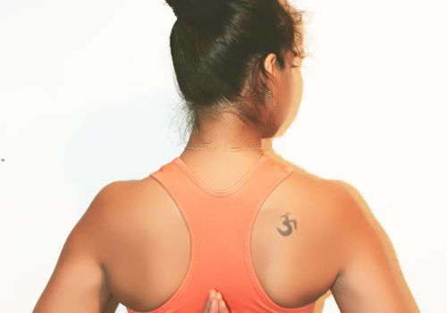 Ung brun kvinne som holder hendene bak ryggen med en om-tatovering på skulderen