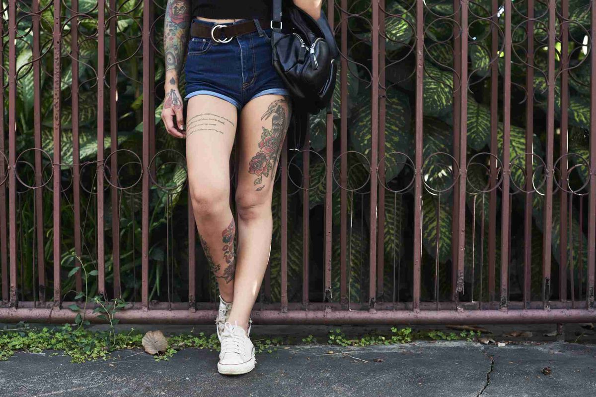 Tatuiruotos moters kojos, stovinčios prieš sodo tvorą